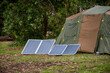 Portable foldable solar panels and Tent at the campsite surrounding by nature. Camping and recreation