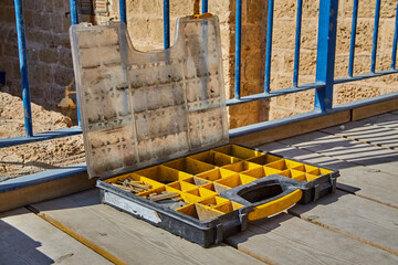 an open soiled box with a variety of nails, screws, nuts, bolts and washers lies on a wooden floor in the open air. Concept for tools and solutions