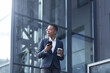 © Liubomir - A confident African-American lady walks around the business district and uses the phone. Holding a cup of coffee, dressed in formal clothes. Attractive businesswoman browsing modern smartphone