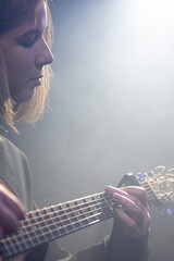 Wall Mural - Young woman playing acoustic guitar in a dark room with haze.