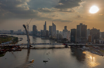 Wall Mural - aerial view of Ho Chi Minh City, Vietnam skyline at sunset with suspension bridge under construction and Saigon river with boats