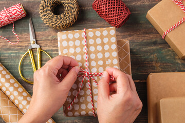 Aufkleber - Hand tied rope on christmas gift box with brown paper decor with pine fir on wood table