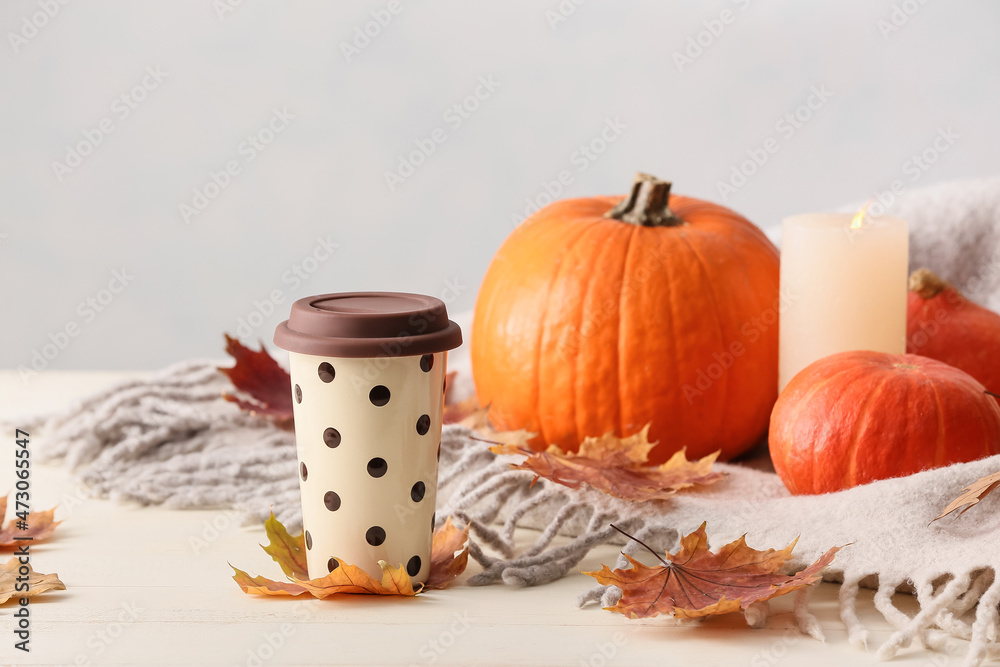 Cup of coffee and pumpkins on light background