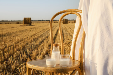 Wall Mural - Natural milk on chair near haystack in harvested field. Picnic with chair, sunflowers, white fabric