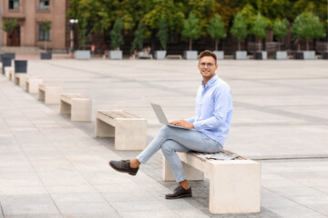 Poster - Handsome young businessman using laptop on city square