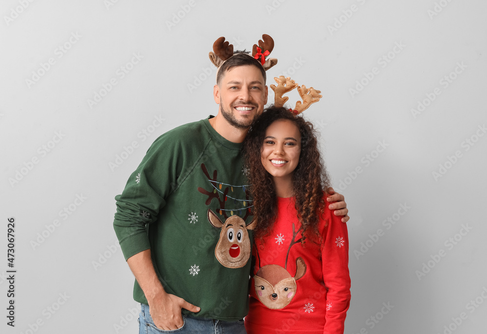 Happy couple in Christmas sweaters on light background