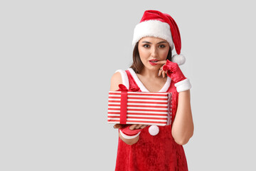 Wall Mural - Sexy young woman in Santa costume and with Christmas gift on light background