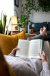 POV of young woman reading a book at home lying on couch. Vertical concept.
