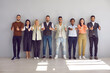 © Studio Romantic - Group portrait of diverse young multiethnic employees in row near wall show thumb up. Smiling multiracial businesspeople recommend good quality company service or business product. Employment.