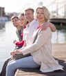 © caftor - group of tourists sitting on embankment dangling legs above the water in port in European city