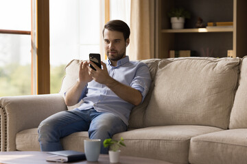Wall Mural - millennial guy with earphones using media app on mobile phone at home, making video call, chatting o