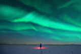 Fototapeta Psy - Tourist with red flashlight on snowy field against the backdrop of incredible starry sky with Aurora borealis. Amazing night landscape. Northern lights in winter field