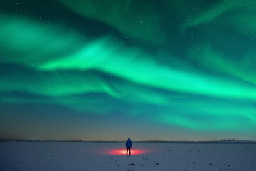 tourist with red flashlight on snowy field against the backdrop of incredible starry sky with aurora