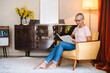 © InsideCreativeHouse - Senior mature elderly caucasian woman housewife relaxing in armchair while reading fashion magazine in living room at home, looking for news information