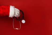 Santa Claus Hand Holding Stethoscope Medical Equipment On Red Background, Copy Space