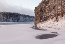 Winter Landscape, Frozen River With A Hole In The Ice, Rocks And Forest On The Bank