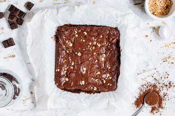 Wall Mural - Top view of cut fudge chocolate brownie in one piece with ingredients by side on a white rustic background
