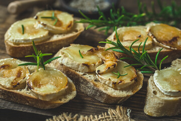 Wall Mural - Baguette bread slices baked with goat cheese and honey, decorated with rosemary, on wooden background