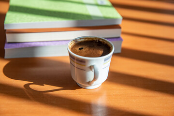 A book and a cup of Turkish coffee on a wooden table with beautiful sunlight