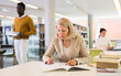 © JackF - Elderly woman makes notes in notebook and read book in public library. High quality photo