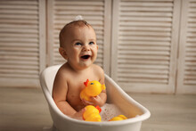 A Baby Of 11 Months Is Bathing In A White Baby Bath With Rubber Ducklings, The Baby Is Laughing, The Concept Of Children's Goods. High-quality Photography