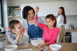 © Halfpoint - Happy small girls with mother and grandmother making pancake mixture indoors at home, cooking.