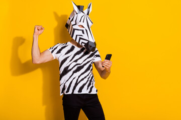 Poster - Photo of excited freak guy blogger in zebra mask use smart phone fist up win followers post isolated over yellow color background