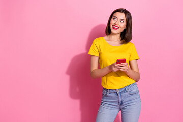 Photo of dreamy cute young lady dressed yellow clothes smiling chatting modern gadget looking empty space isolated pink color background