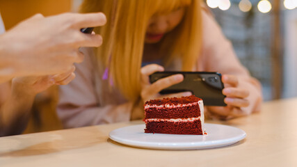 Cheerful young Asia friend using phone taking a photograph food and cake at coffee shop. Two joyful attractive Asian lady together at restaurant or cafe. Holiday activity, or modern lifestyle concept.