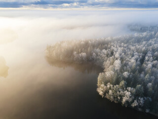 Wall Mural - Aerial view over frozen lake in a misty forest, Finland. Winter season. View from above water surface, frozen trees and low fog clouds landscape...