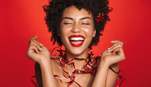 Happy African Woman Laughs And Smiles, Body Decorated With Christmas Gift Wrap. Girl Enjoys Winter Holidays Sale, Special Promo, Standing Over Red Background