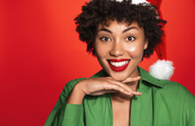 Christmas And Winter Holidays, Women Beauty. Smiling Black Woman With Red Lips, Makeup And White Teeth, Wearing Santa Claus Hat And Looking Happy, Red Background