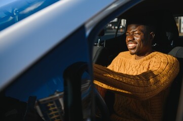 Wall Mural - Handsome young African American man in his new high-tech electric vehicle while drinking. Self driving vehicle concept