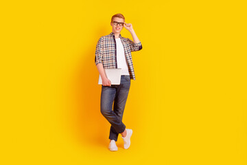 Full body photo of young cheerful guy hand touch eyeglasses hold laptop isolated over yellow color background