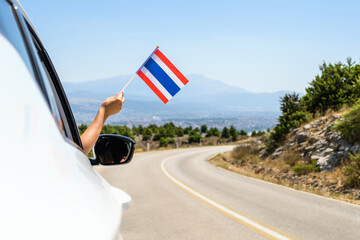 Wall Mural - Woman holding Thailand flag from the open car window driving along the serpentine road in the mountains. Concept