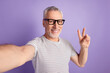 © Tetiana - Photo of handsome retired man take selfie show peace cool v-symbol isolated over violet color background