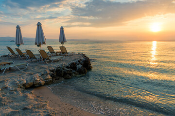 Wall Mural - Beautiful sunset seascape with beach chairs and umbrella on the coast, Greece