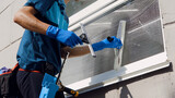 Male professional cleaning service worker in overalls cleans the windows and shop windows of a store with special equipment