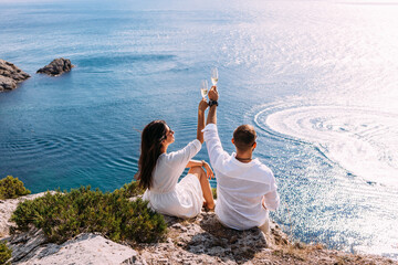 A couple in love celebrates their engagement on the seashore. A beautiful couple drinks champagne by the sea. Honeymoon trip. Lovers on the beach. Wedding travel. Couple on vacation. Copy space