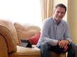 © Mint Images - Man sitting on sofa smiling at camera.