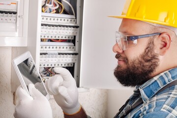 Canvas Print - Electrician at work on an electrical panel protected in safety goggles and gloves; Coronavirus. Construction industry. Covid 19 Prevention.