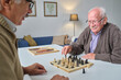 © pressmaster - Two elderly men playing chess together at the table during leisure time in nursing home