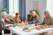 © pressmaster - Group of elderly friends eating pizza at the table after board game in the living room