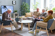 © pressmaster - Senior people reading a book, watching TV and talking to each other during their leisure time in nursing home