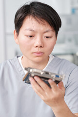 Poster - Serious female technician looking at hardware in her hand while repairing it in workshop