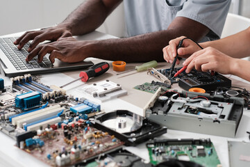 Poster - Hands of young intercultural coworkers typing on laptop keypad and soldering circuit board by desk