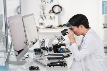 Poster - Young Asian female researcher looking in microscope while making scientific investigation of hardware