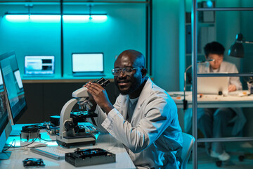Poster - Young successful researcher with microscope sitting by workplace in scientific laboratory