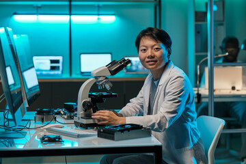 Poster - Young successful chinese female researcher with microscope looking at camera by workplace in laboratory