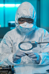 Poster - Young African man in protective gloves, eyeglasses and coveralls looking at microchip in magnifying glass